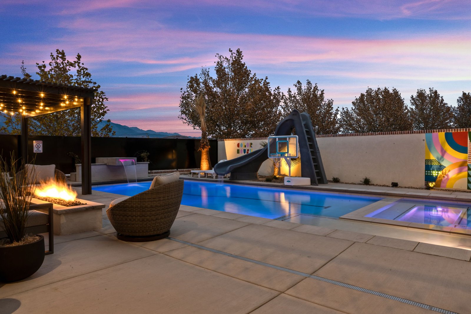 Wide view of the Color House backyard: fire pit, pool, waterslide, basketball hoop and mural at sunset