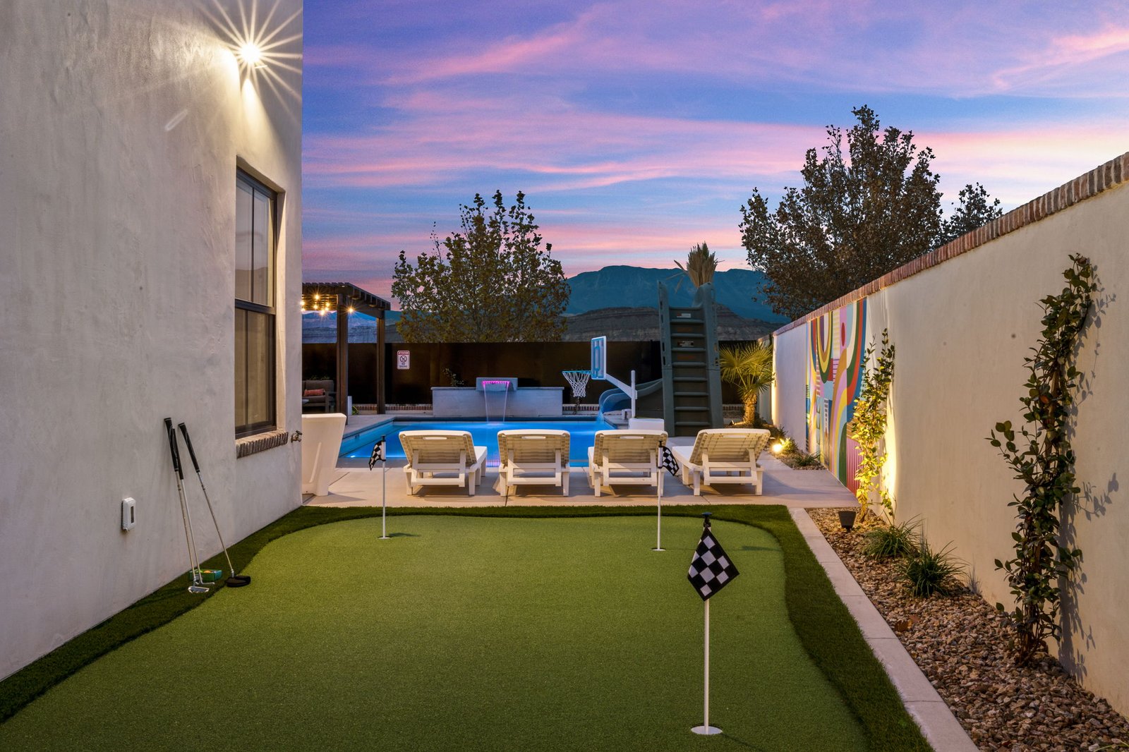 Putting green at Color House at twilight with pool, loungers and mural beyond